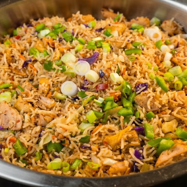 Close-up of chicken fried rice with green onions, bell peppers, and purple cabbage in a metal bowl.