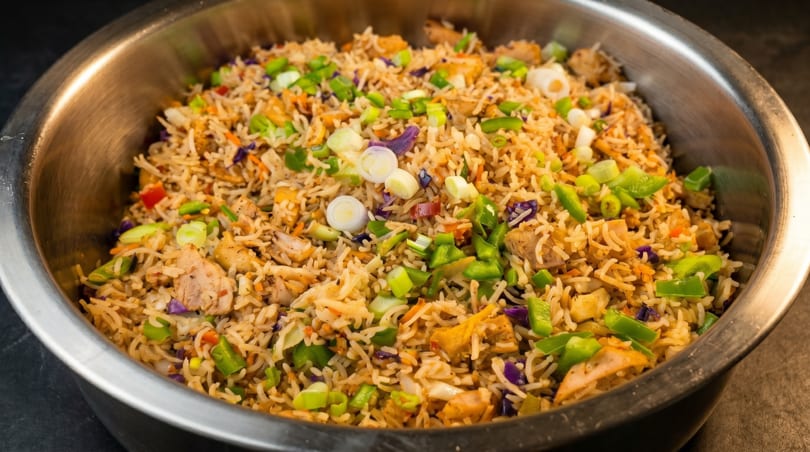 Close-up of chicken fried rice with green onions, peppers, and purple cabbage in a metal bowl.